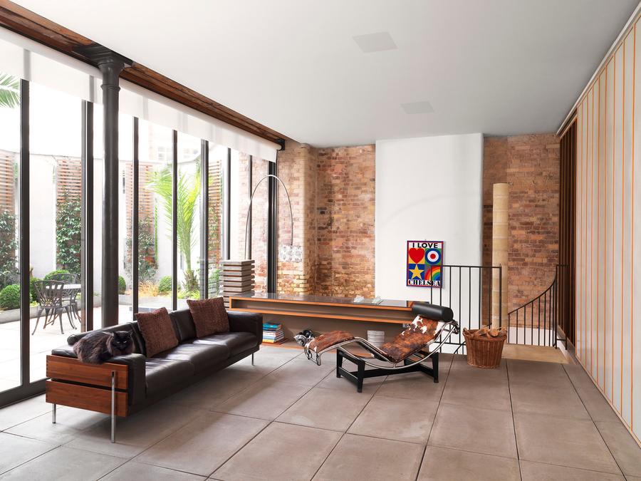 Loft-style living room with exposed brick walls, leather sofa, chaise lounge, and in-ceiling B&W speakers.