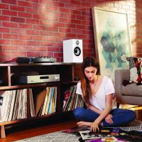 Woman looks through vinyl records while sitting on the floor in front of an AV stand